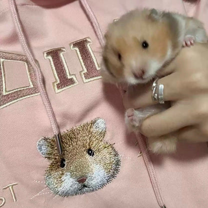 Person holding a small animal next to a pink hoodie with a hedgehog design.